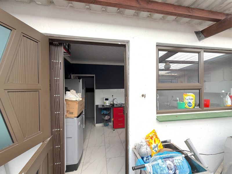 A functional scullery area featuring tiled flooring, aluminium window frames, and direct access to the exterior through a folding security gate.