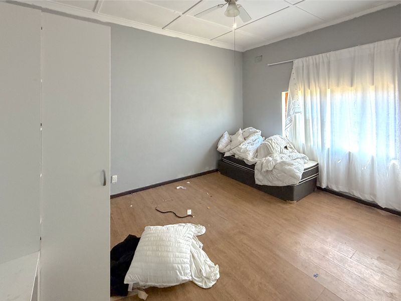 A bedroom featuring laminate flooring, a built-in wardrobe, and a ceiling fan, requiring cosmetic updates to improve its overall condition.