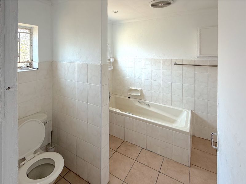 A functional bathroom featuring a built-in bathtub, tiled walls and flooring, and a separate toilet area, offering a blank canvas for renovation.