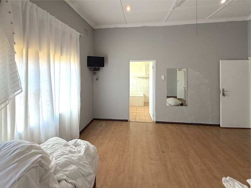 A spacious bedroom featuring laminate flooring, recessed ceiling lighting, and direct access to an en-suite bathroom.