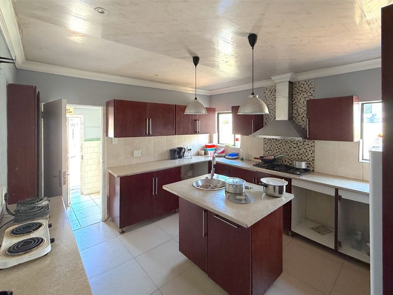 A functional kitchen featuring dark wood cabinetry, a central island with a sink, gas hob, extractor fan, and tiled backsplash.
