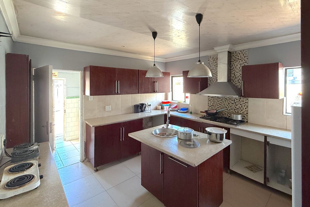 A functional kitchen featuring dark wood cabinetry, a central island with a sink, gas hob, extractor fan, and tiled backsplash.