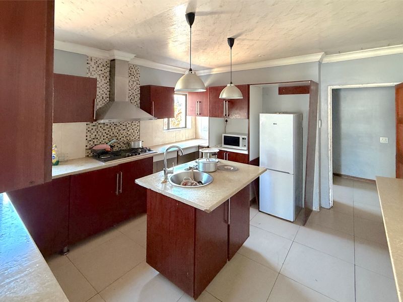 A functional kitchen featuring dark wood cabinetry, a central island with a sink, gas hob, extractor fan, and mosaic tile backsplash.