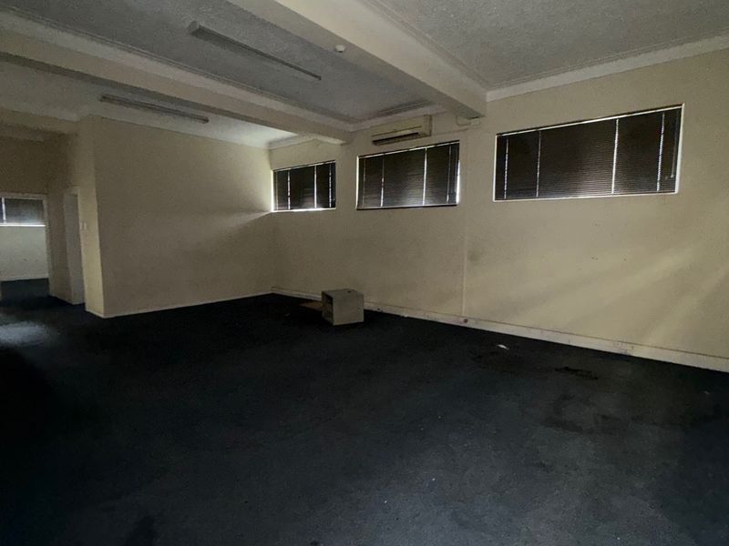 An empty, open-plan office space featuring carpeted flooring, fluorescent lighting, and wall-mounted air conditioning, suitable for various industrial or commercial business applications.