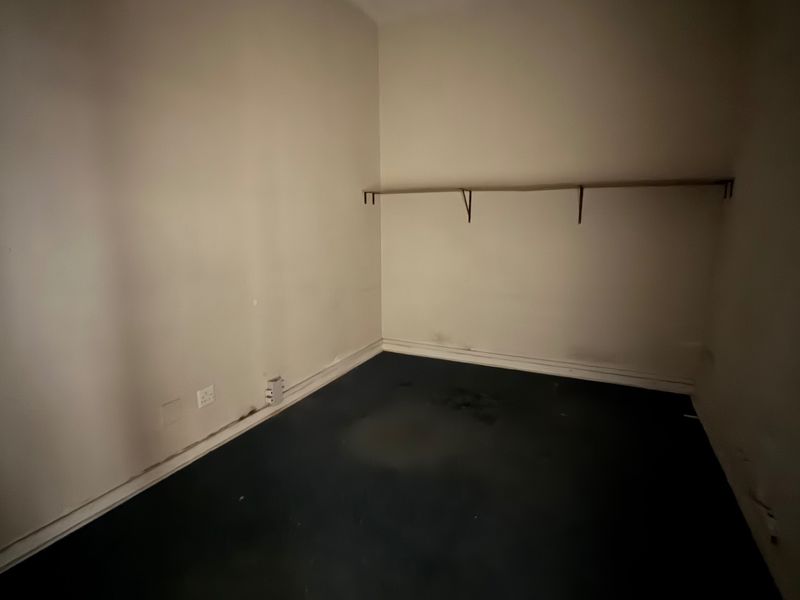 An empty, utilitarian office space featuring dark flooring, wall-mounted shelving, and basic overhead lighting, suitable for renovation or workspace customization.