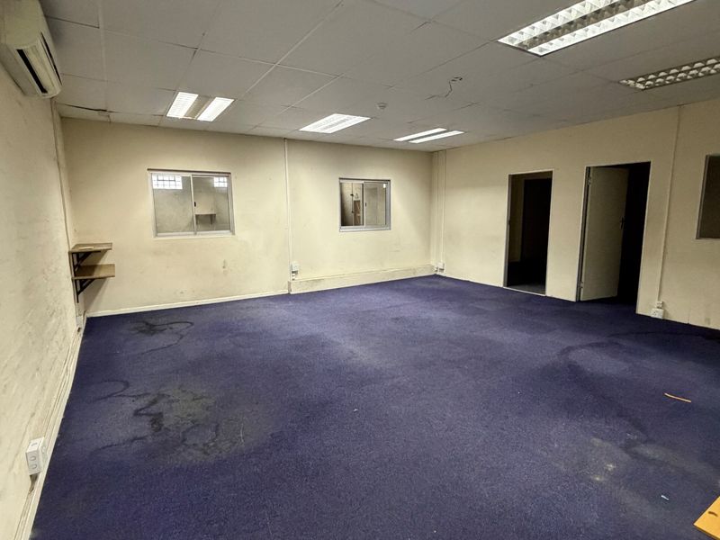 An empty industrial office space featuring suspended ceilings, fluorescent lighting, split-system air conditioning, and carpeted flooring.
