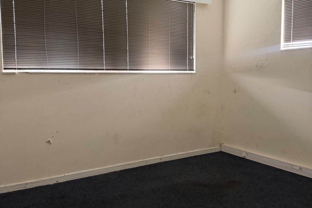 An empty bedroom featuring dark carpet flooring, venetian blinds, and coved ceilings, currently requiring cosmetic updates to the wall surfaces and flooring.