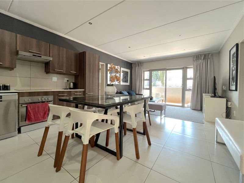 Open-plan living and kitchen area featuring modern cabinetry, built-in appliances, tiled flooring, and direct access to a balcony through sliding glass doors.