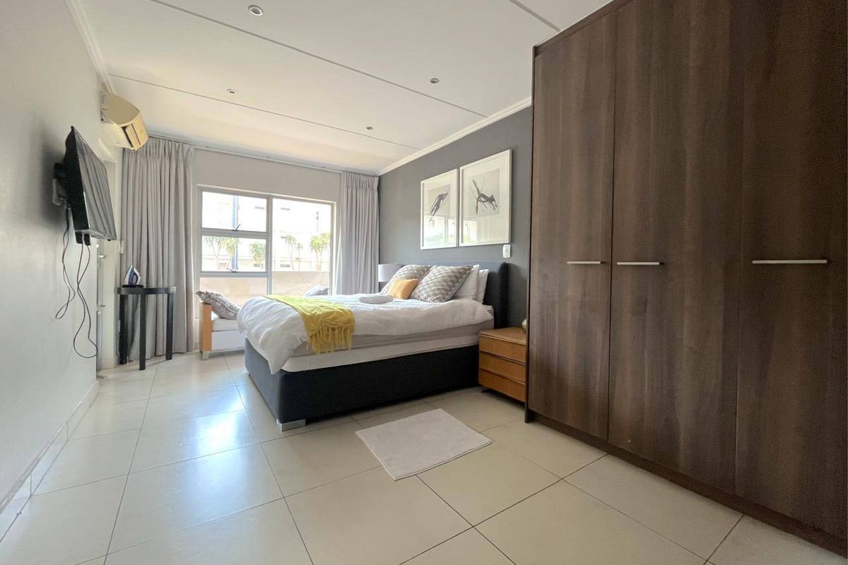 A spacious bedroom featuring large built-in wardrobes, neutral tiled flooring, recessed ceiling lighting, and an integrated air conditioning unit.