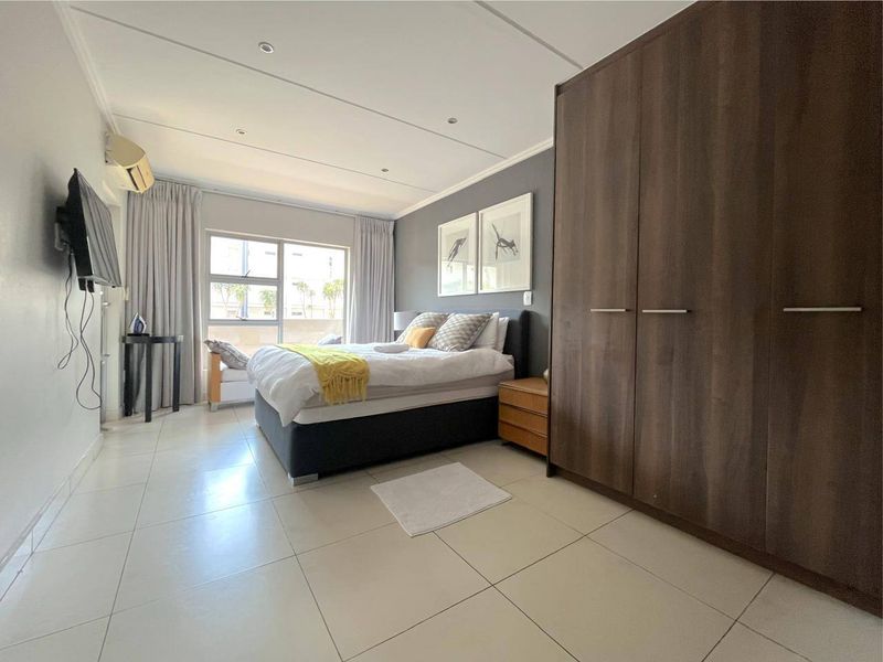 A spacious bedroom featuring large built-in wardrobes, neutral tiled flooring, recessed ceiling lighting, and an integrated air conditioning unit.