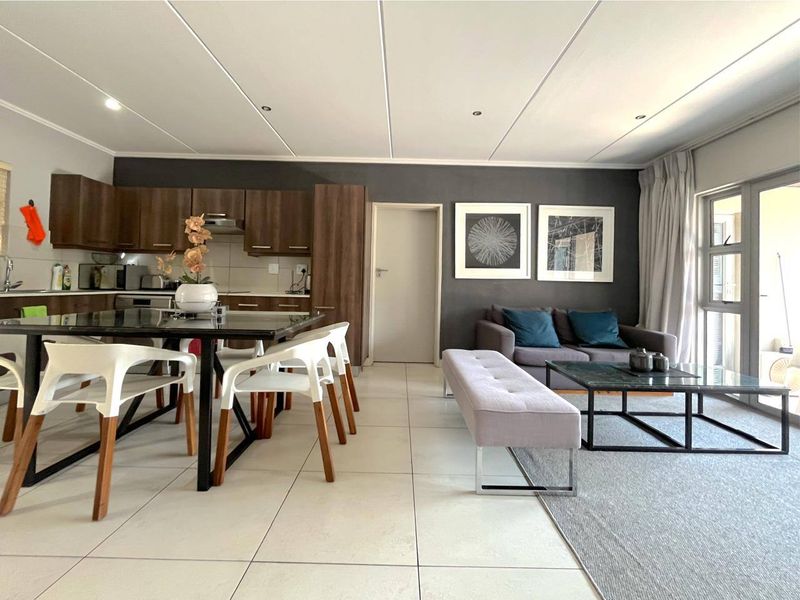 Modern open-plan living area featuring a well-appointed kitchen with dark wood cabinetry, tiled floors, and seamless access to an outdoor balcony.