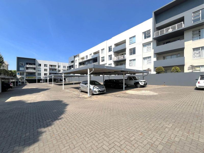 Exterior view of a modern apartment complex featuring paved parking areas with covered bays and multi-story residential units with balconies.