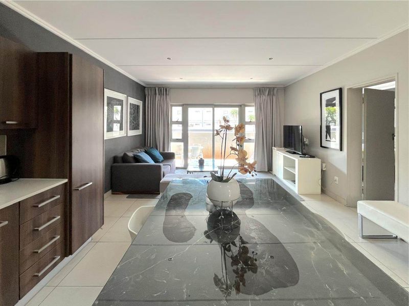 Modern open-plan living area featuring a sleek kitchen with stone countertops, tiled floors, and large sliding doors leading to a balcony.