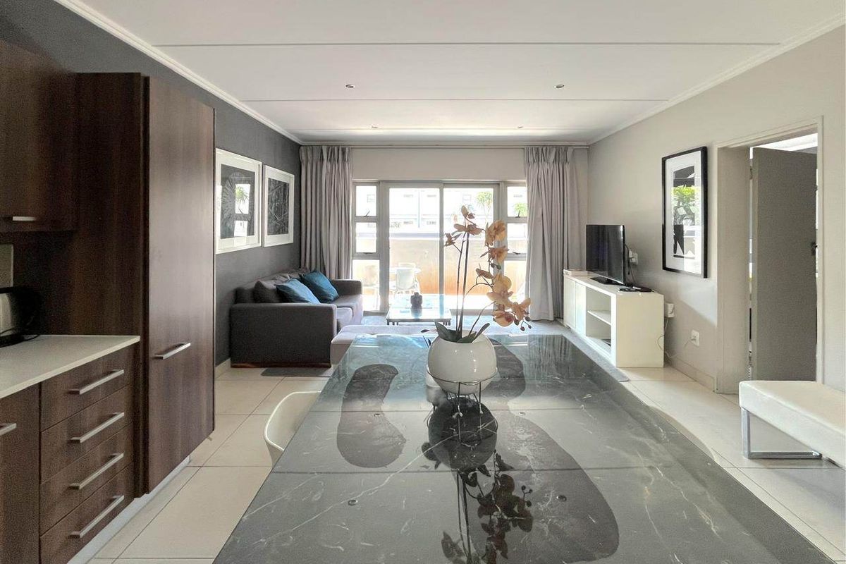 Modern open-plan living area featuring a sleek kitchen with stone countertops, tiled floors, and large sliding doors leading to a balcony.