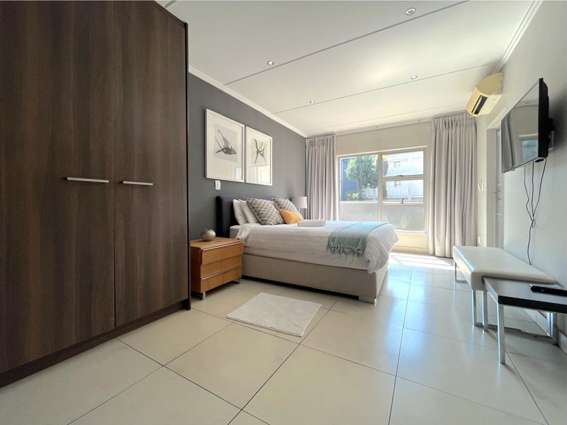 A well-maintained bedroom featuring tiled flooring, recessed ceiling lighting, a built-in wardrobe, and a wall-mounted air conditioning unit.