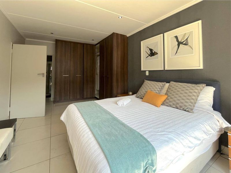 A well-maintained bedroom featuring dark wood built-in cupboards, neutral tiled flooring, and a modern dark accent wall.