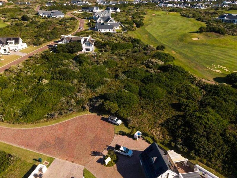 Aerial view of a vacant residential plot situated within a coastal estate, featuring established vegetation and proximity to a golf course.