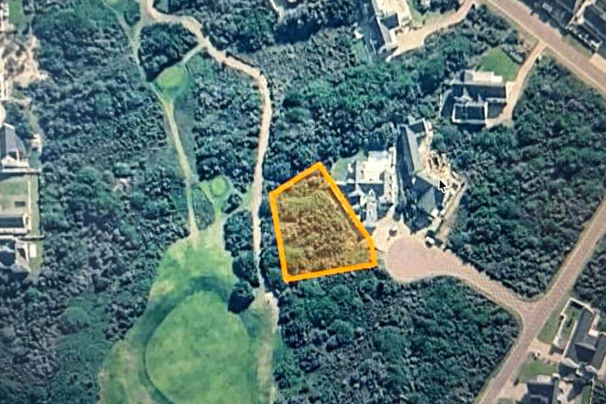 An aerial view of a vacant residential land plot highlighted in orange, situated within a landscaped estate environment.