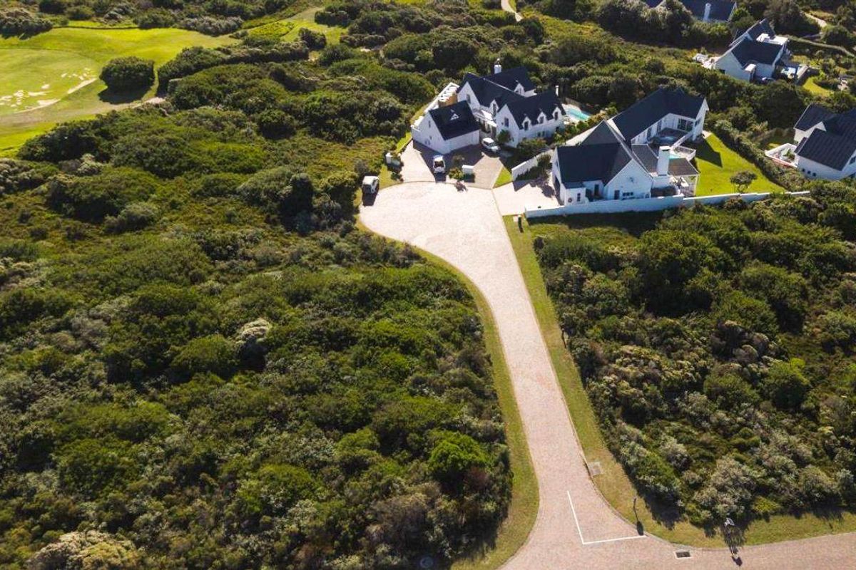 Aerial view of a residential property featuring a long paved driveway, multiple pitched roof structures, a swimming pool, and surrounding natural vegetation.