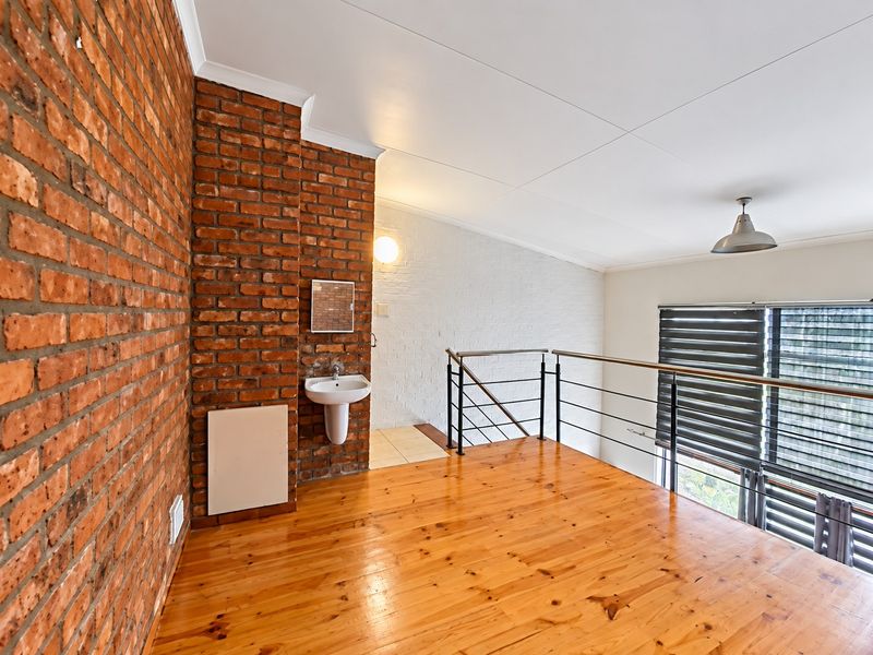A mezzanine level bedroom area featuring exposed brick walls, timber flooring, a built-in pedestal basin, and a metal balustrade overlooking the lower level.