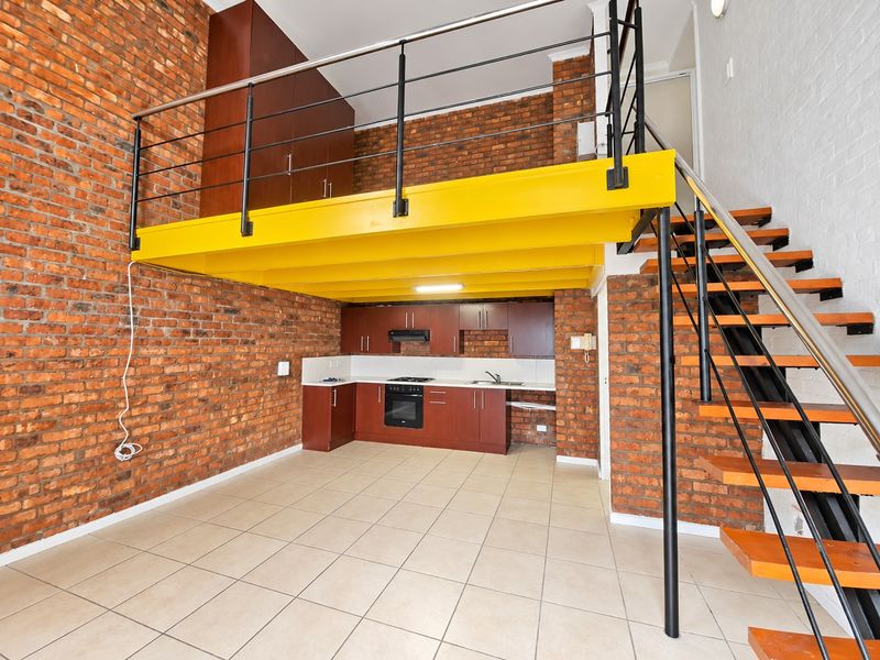 Open-plan kitchen and living area featuring exposed brick walls, a mezzanine level with a steel staircase, and functional built-in cabinetry.