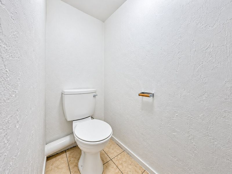 A compact, functional powder room featuring a standard toilet, tiled flooring, and a wall-mounted toilet roll holder.