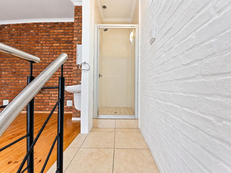 A clean bathroom area featuring a shower enclosure, wall-mounted basin, and a mix of exposed and painted brick walls with tiled flooring.