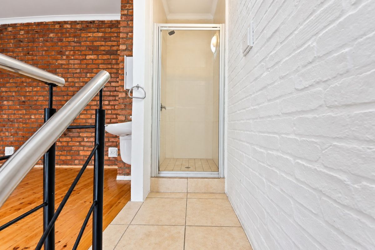 A clean bathroom area featuring a shower enclosure, wall-mounted basin, and a mix of exposed and painted brick walls with tiled flooring.