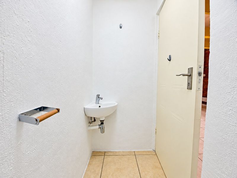 A compact guest cloakroom featuring a wall-mounted basin, tiled flooring, and a neutral interior door.