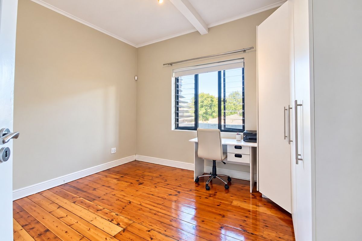 A bright bedroom featuring polished timber flooring, a built-in wardrobe, and a louvre window providing natural light.