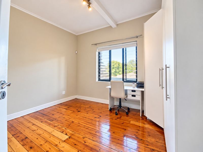 A bright bedroom featuring polished timber flooring, a built-in wardrobe, and a louvre window providing natural light.