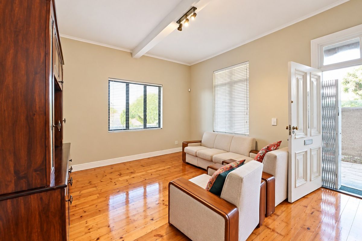 A bright living room featuring polished hardwood flooring, an exposed ceiling beam, and direct access to an outdoor area through a panelled entrance door.