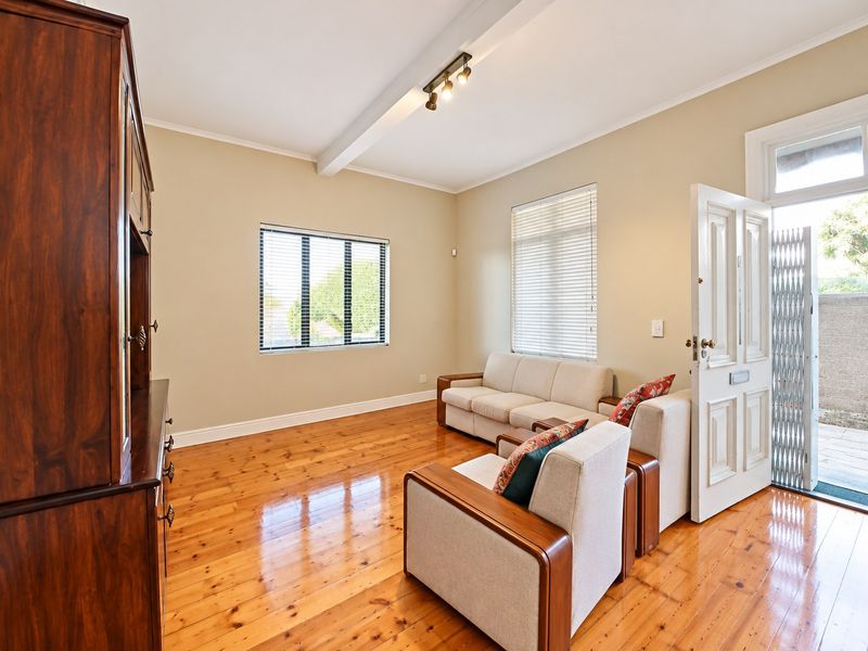 A bright living room featuring polished hardwood flooring, an exposed ceiling beam, and direct access to an outdoor area through a panelled entrance door.