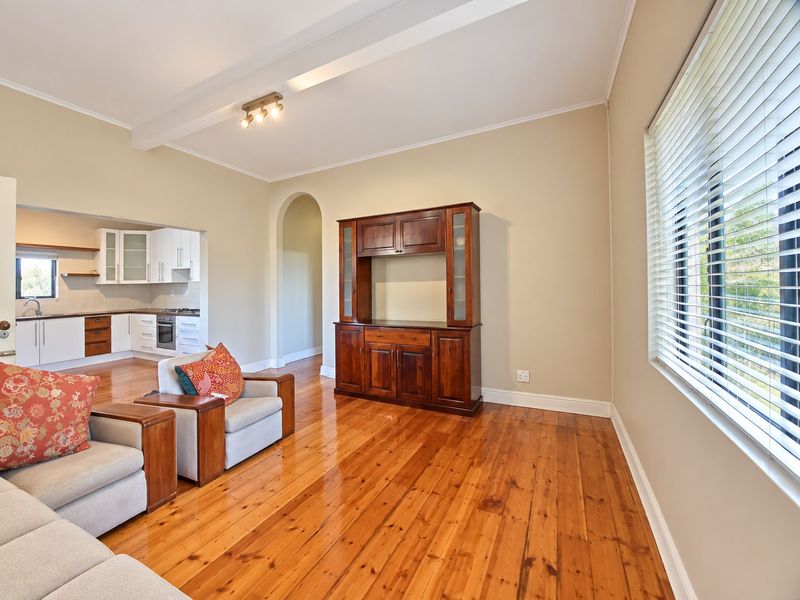 Spacious open-plan living area featuring polished hardwood floors, an arched transition to the kitchen, and large windows with fitted venetian blinds.