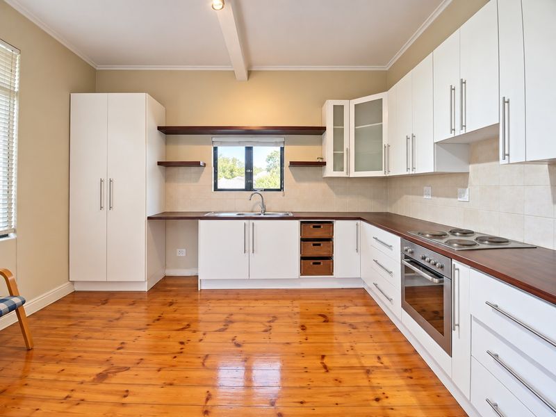 A clean, well-maintained kitchen featuring white cabinetry, dark laminate countertops, stainless steel appliances, and polished timber flooring.