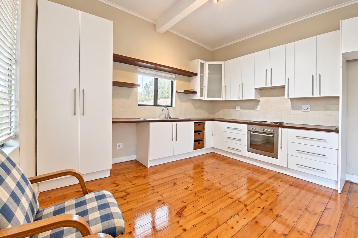A well-maintained kitchen featuring white cabinetry, dark laminate countertops, built-in oven, hob, and polished timber flooring.