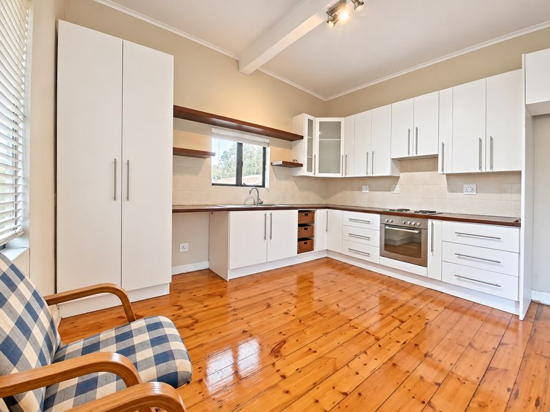 A well-maintained kitchen featuring white cabinetry, dark laminate countertops, built-in oven, hob, and polished timber flooring.