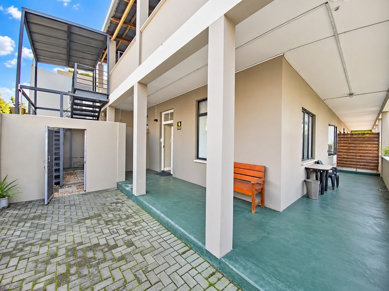 A covered rear patio area featuring painted concrete flooring, an external staircase, and a timber privacy screen, providing access to the apartment entrance.
