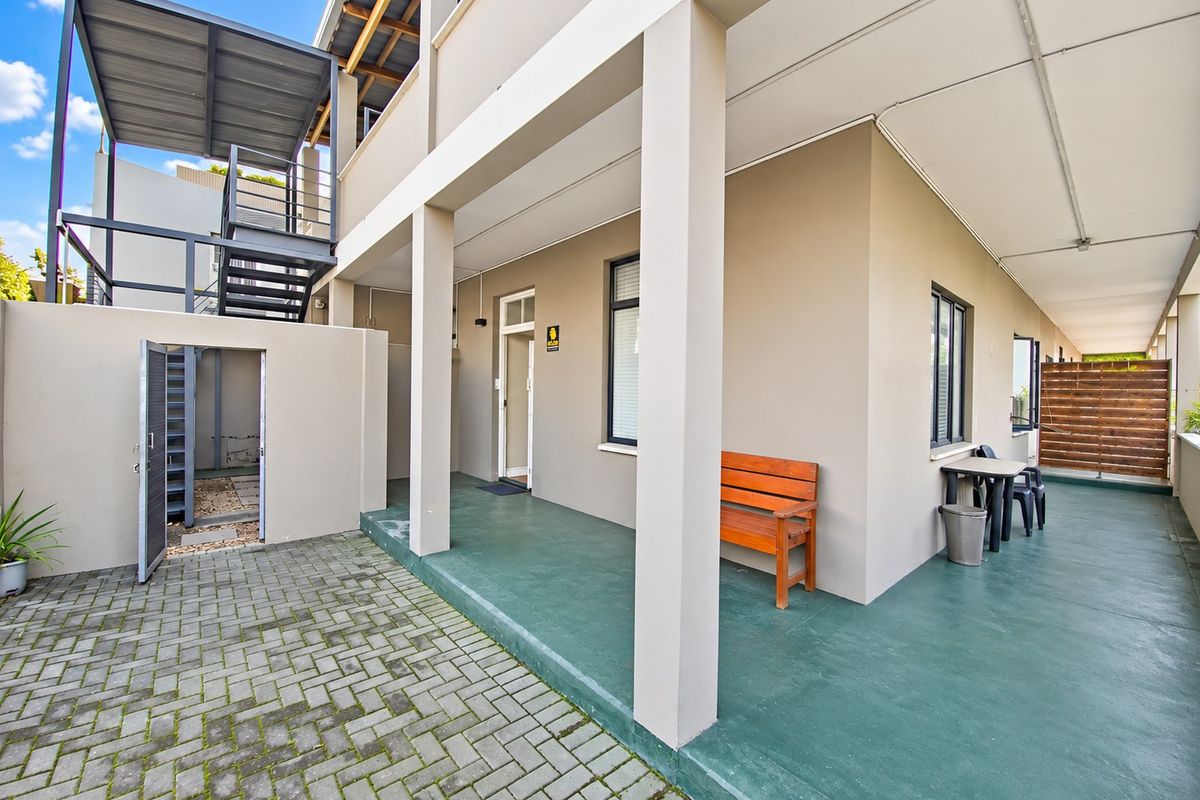 A covered rear patio area featuring painted concrete flooring, an external staircase, and a timber privacy screen, providing access to the apartment entrance.