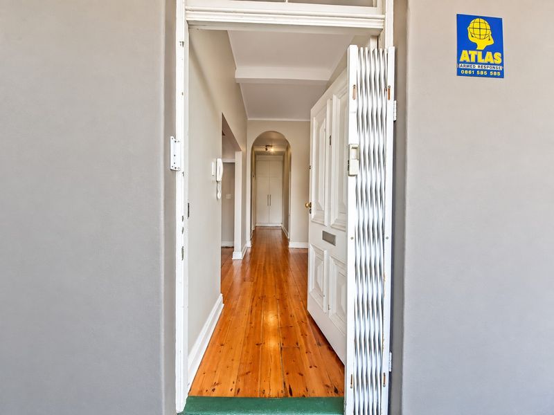 An inviting apartment entrance featuring polished timber flooring, a secure gate, and a classic archway leading into a hallway with built-in storage.
