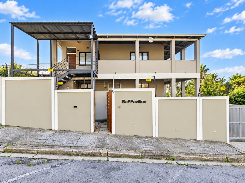 Front elevation of Bay Pavilion apartment complex featuring a secure perimeter wall, electric fencing, and an external metal staircase leading to upper-level balconies.