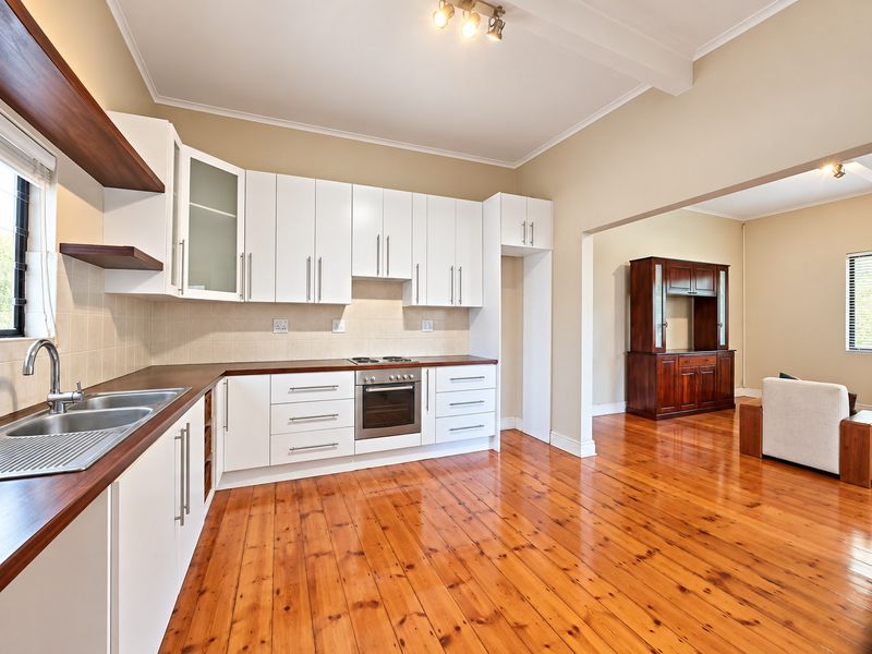 Open plan kitchen featuring white cabinetry, dark wood countertops, and polished hardwood flooring, seamlessly flowing into the adjacent living area.