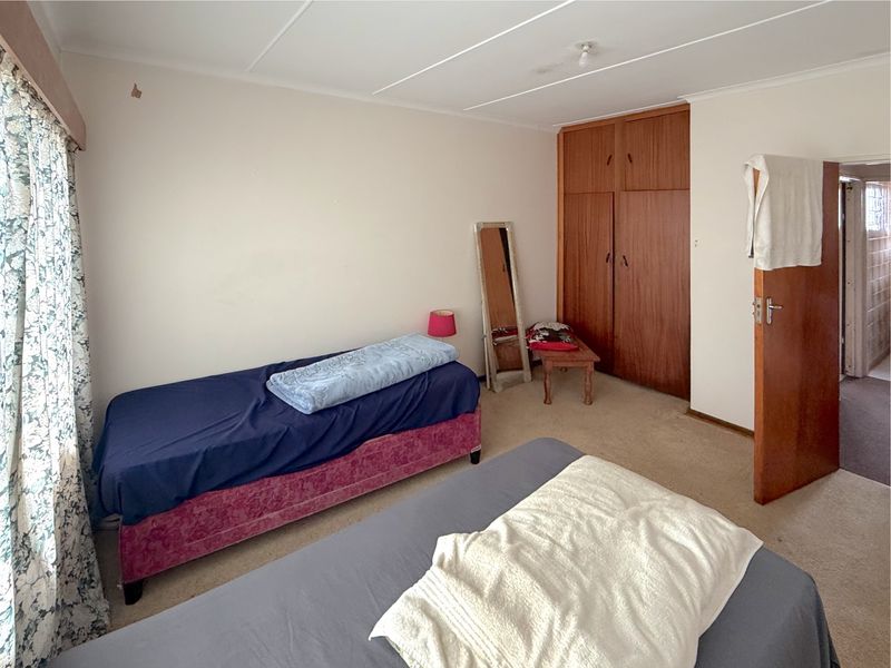 A bedroom featuring built-in wooden wardrobes and carpeted flooring, offering a functional space with potential for cosmetic updates.