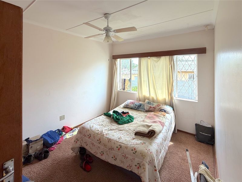 A bedroom featuring a ceiling fan, security bars on the windows, and carpet flooring. The room requires cosmetic updates to improve its overall condition.