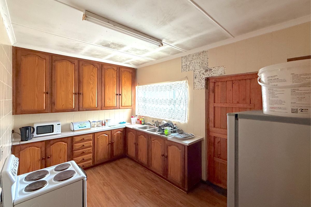 A dated kitchen featuring wooden cabinetry, laminate countertops, and a stainless steel sink, requiring cosmetic updates to modernize the space.