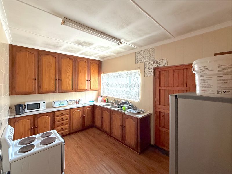 A dated kitchen featuring wooden cabinetry, laminate countertops, and a stainless steel sink, requiring cosmetic updates to modernize the space.