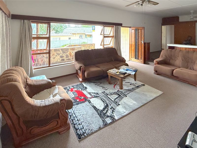Spacious living room featuring a large picture window, neutral carpeting, and a ceiling fan, offering a bright and functional layout.