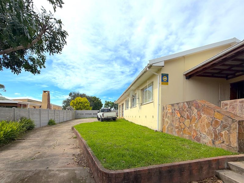 Rear exterior view of the property featuring a concrete driveway, a small lawn area with a brick retaining wall, and stone cladding accents.