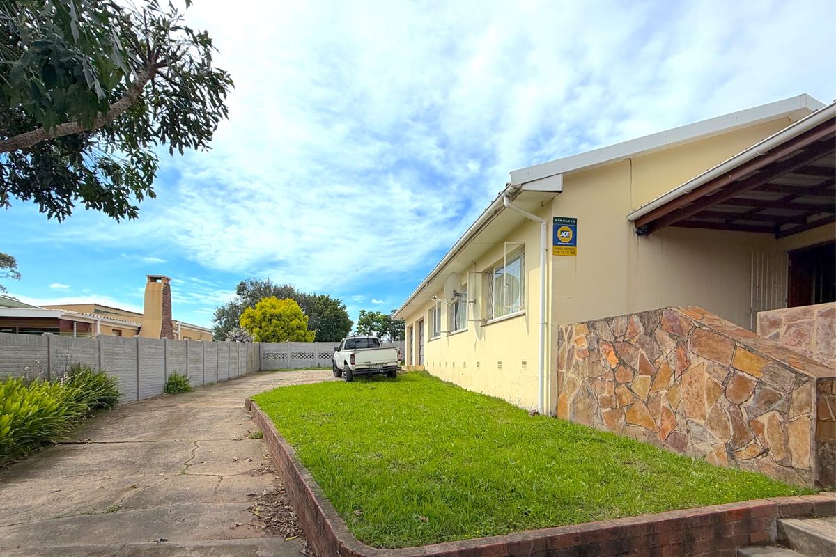 Rear exterior view of the property featuring a concrete driveway, a small lawn area with a brick retaining wall, and stone cladding accents.