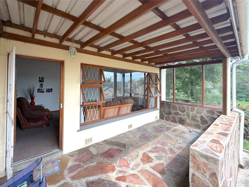 A covered patio featuring flagstone flooring, exposed timber beams, and stone masonry walls, providing a rustic outdoor living space with views.